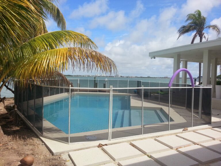 White removable mesh pool safety fence installed around a waterfront swimming pool