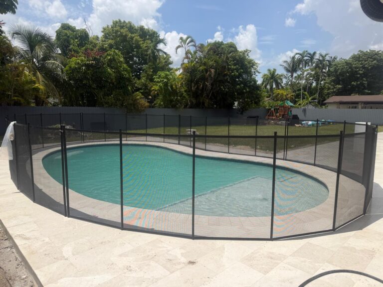 Black removable mesh pool safety fence installed around a curved residential swimming pool