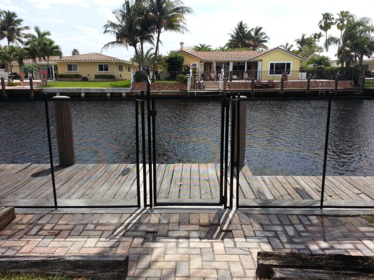 Black removable mesh pool fence with gate installed along a residential waterfront seawall