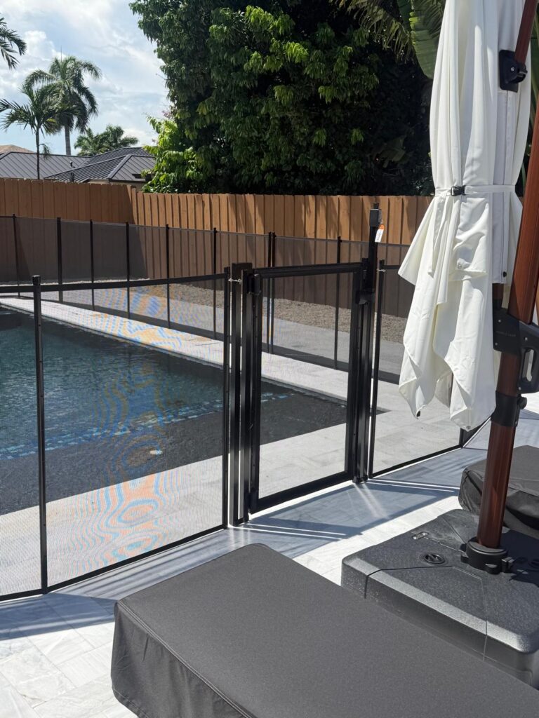 Black removable mesh pool fence with a framed safety gate installed beside a residential pool
