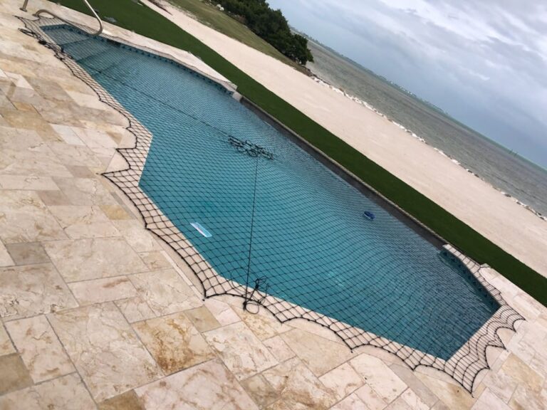 Black pool safety net installed over a waterfront swimming pool with a beach view