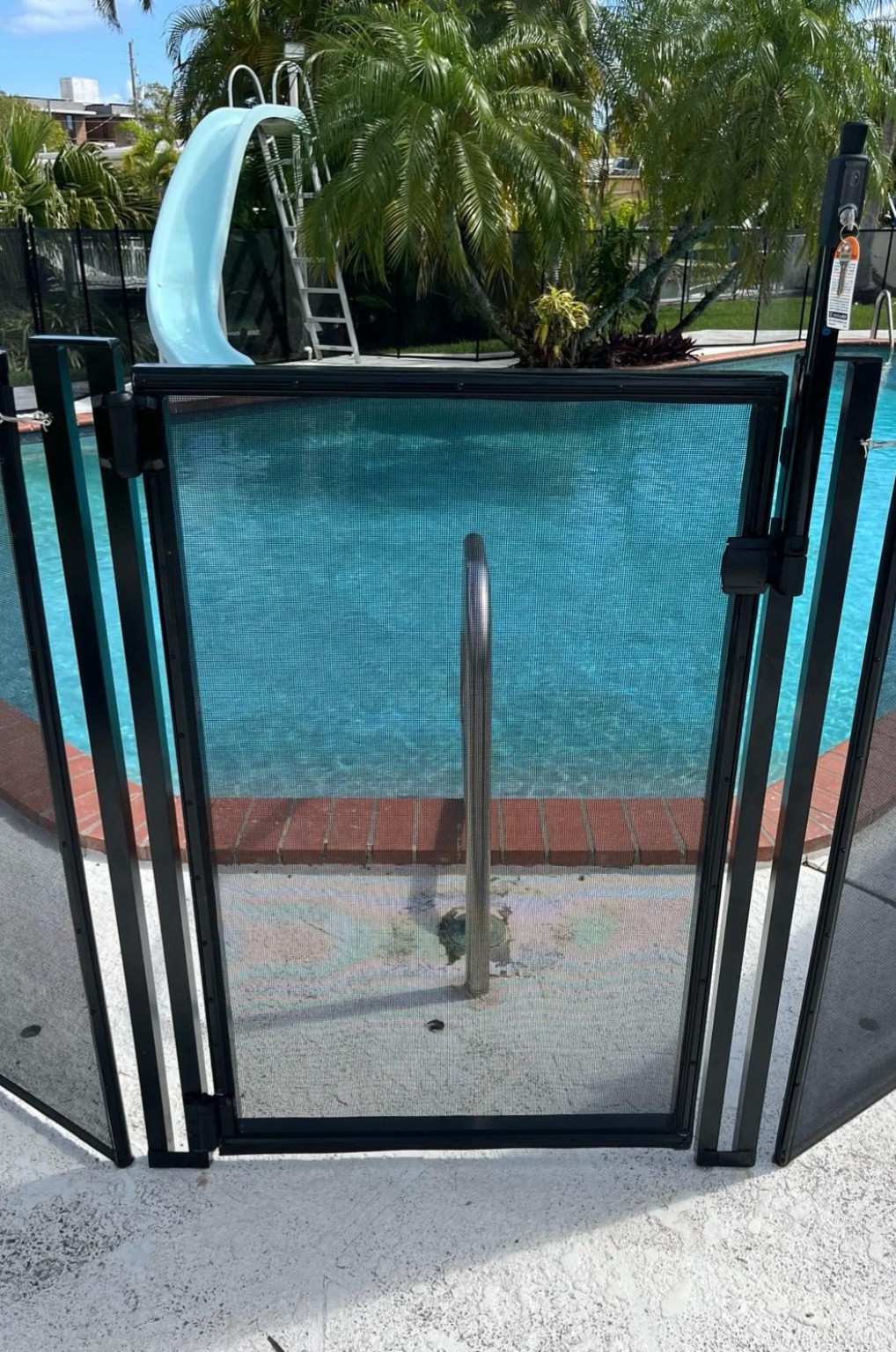 Black self-closing pool gate with MagnaLatch beside a swimming pool