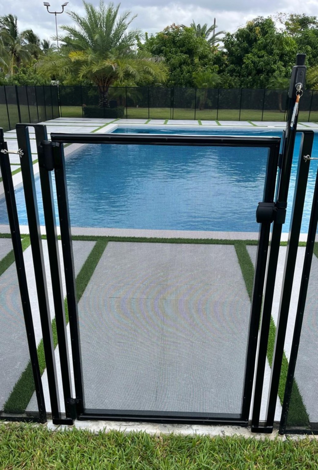 Black self-closing pool gate installed on a pool deck