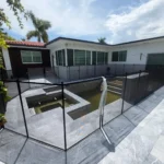 Modern backyard with a sunken rectangular pool pit, surrounded by a black glass-panel fence on a gray tiled deck.