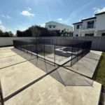 Empty rectangular pool pit surrounded by a black safety fence in a modern backyard setting.