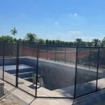 Under-construction empty swimming pool surrounded by black temporary safety fencing on a sunny day